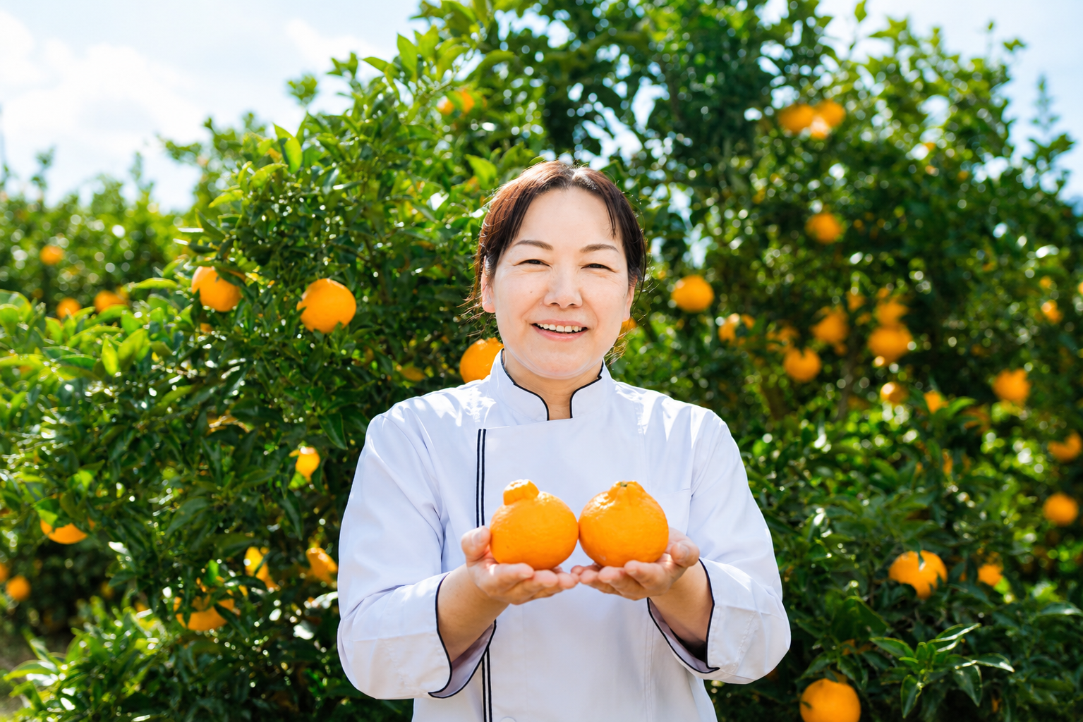 柑橘畑で柑橘を手にする店主・パティシエの原山奈美
